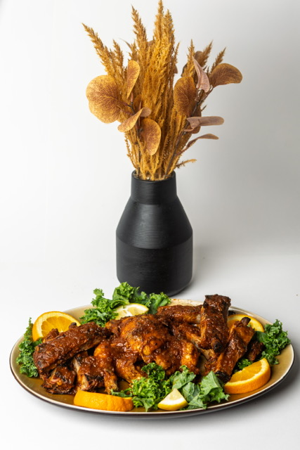 A platter of sauced wings beside a vase of dried grasses