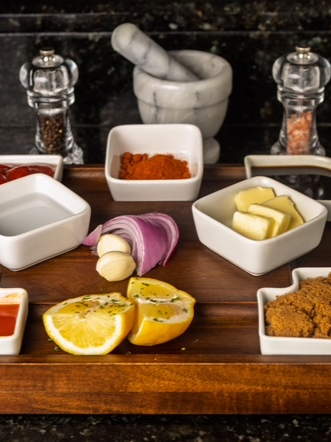 Spices, lemon, onion and garlic laid out on a wooden board